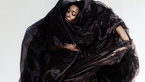 Artistic photo of a Black femme dancer contorted and wrapped in black guaze.