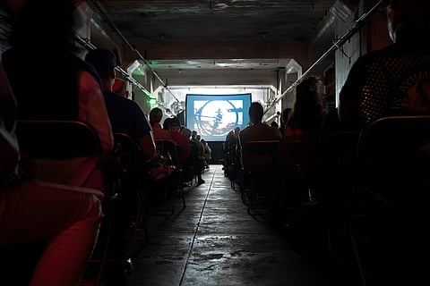 Darkened makeshift theater with viewers watching a short film on a projected screen.