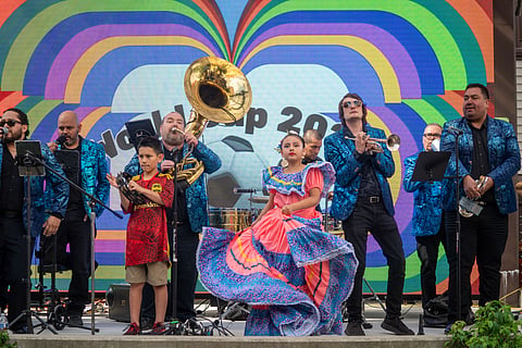 Band and young dancers perform in front of World Cup artwork on screen.