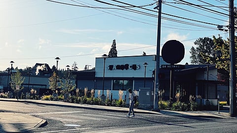 Closed Starbucks in Rainier Beach with covered signs and a pedestrian crossing the street in front.