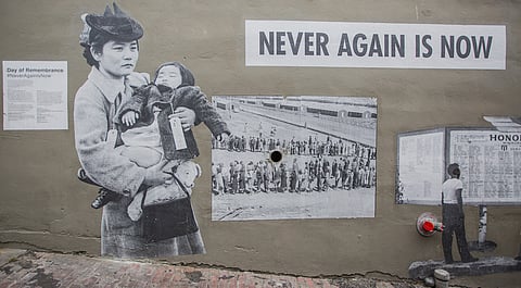 A painted wall that reads "Never Again Is Now" along with painted black-and-white vintage photos of Japanese American incarceration.