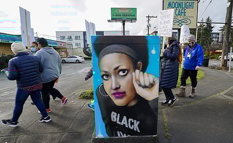 A couple dozen medical staff from Carolyn Downs Family Medical Center and Country Doctor Community Health Centers walk past a signal box painted with a portrait of community activist Rahwa Habte on their way to protest in front of Raleigh Watts' home. (Photo: Susan Fried)