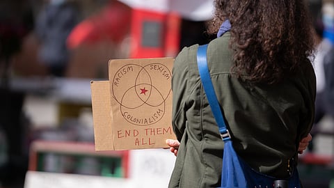 Protestor stands with a sign that reads, "Racism, Sexism, Colonialism. END THEM ALL." (Photo: Chole Collyer)