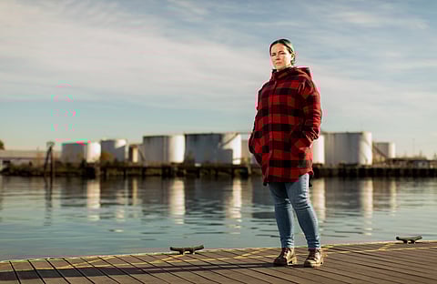 Melissa Malott, executive director of Communities for a Healthy Bay, poses on Commencement Bay in Tacoma, Washington, Monday, November 8, 2021. A storage facility for fossil fuels is visible in the background. (Photo: Dan DeLong/InvestigateWest)