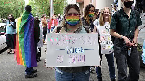 Among a crowd of protesters, an SPU student wearing a rainbow mask holds a sign labeled "LGBTQ+ Staff Belong at SPU!!" Many queer students, staff, and allies made their dissent heard after the SPU board voted to maintain homophobic employment policies. (Photo: Guy Oron)
