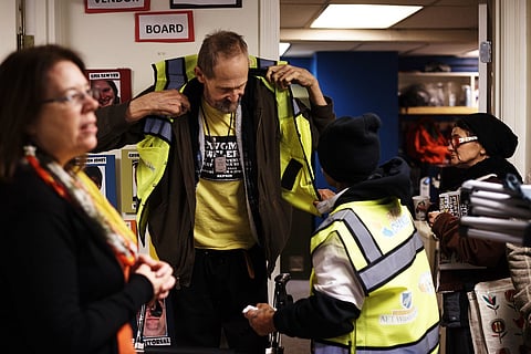 Real Change vendors try on their new official vests, December 2017. Real Change has been a source of no-barrier work for people experiencing homelessness and poverty for over 25 years in the Seattle area, and yet people still believe that their neighbors who are unhoused do not want to work. (Photograph via the Real Change archives.)