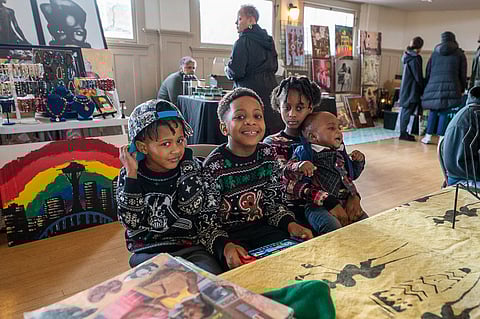 Four youth wearing "ugly Christmas sweaters" smiling at the Soul Holiday Market.