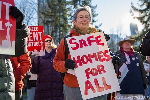 Seattle housing protest featuring an older woman holding a “Safe Homes For All” sign, with others demanding rent control.