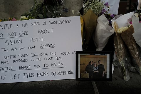 A photo of Eina (middle) and Sung Kwon surrounded by flowers and signs of anger and sorrow. (Photo: Maile Anderson)