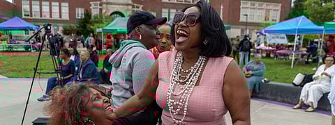 Karen Jones in a black blouse and riding a motorized scooter hugging Josephine Howell in a pink dress.