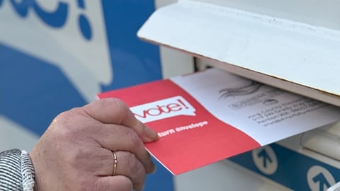 A voter drops their completed ballot into a King County Elections drop box. (Photo: Megan Christy)