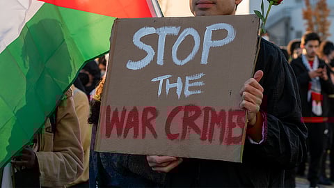 A protestor holds a sign calling for the end of Israel's war crimes against Palestinians during a march to the Boeing Military Delivery Center in November 2023. (Photo: Susan Fried)