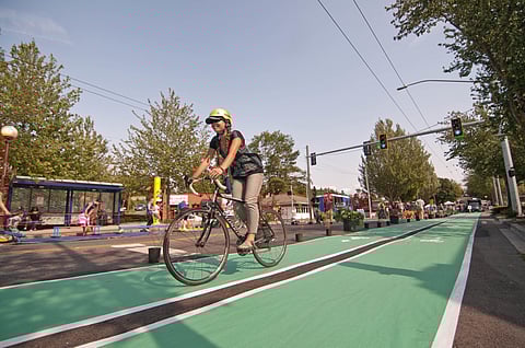 A bicyclist rides down the street during Rainier Valley Summer Streets in 2014. (Photo is attributed to SDOT Photos, under a Creative Commons, CC BY-NC 2.0 DEED license.)