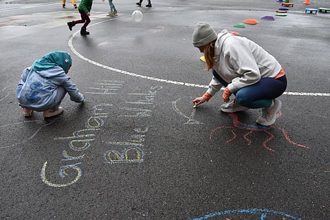 Katie Kribbs, a parent whose son attends Graham Hill Elementary School, traces the chalk drawing of the school's mascot as students play around her during Move-A-Thon Saturday, April 27. The Southeast Seattle Schools Fundraising Alliance holds a two-week-long fundraising effort for South Seattle schools that encourages students and parents to move and to donate. (Photo: Phil Manzano)