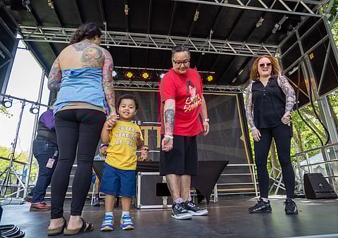 The three finalists in the tattoo portrait competition, Elsa, Robert, and Tierra, show off their tattoos to the audience while the judges decide on the winner. (Photo: Susan Fried)