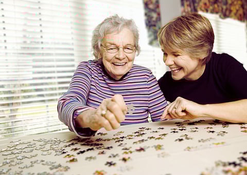 An older woman with her caregiver with a jigsaw puzzle.