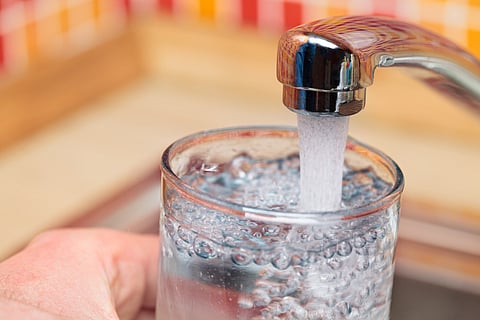 A faucet filling a water glass.
