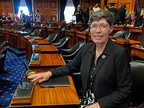 State Representative Joan Meschino sitting at her desk in the wood paneled state house chamber.