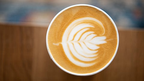 Hot coffee latte with feathered art in the milk foam with a wooden background