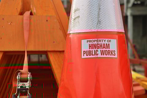An orange safety cone with a label that says "Property of Hingham Public Works" on it.