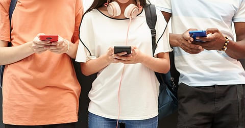 Three students stand holding their cell phones in their hands, looking down but you cannot see their faces or heads. A school committee meeting discussing the impact of Cohasset High School’s phone policy on student engagement.