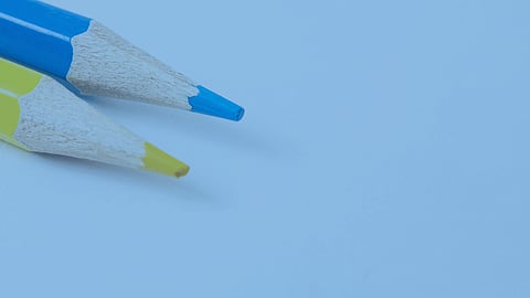 Blue and yellow colored pencils are on a blue background- Norwell School Committee members discuss the FY26 budget and its reliance on an override for funding.