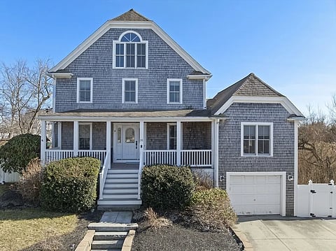 A grey shingled expanded cape house with white trim and a 1 car garage.