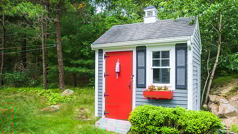 Little blue cottage with red door in a backyard