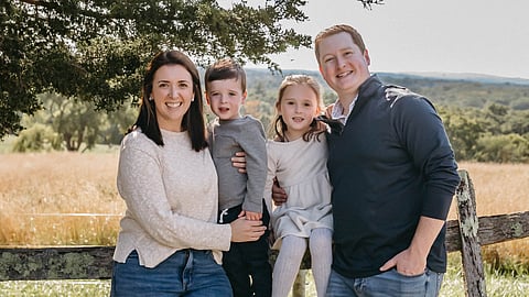 John McGrath and family pose in front of a field and post and rail fence