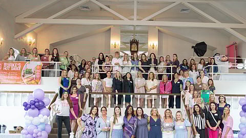 A group of women stand with purple balloons in a ball room during a women in business conference