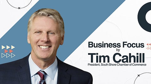 A white man wearing a black suit with a red patterned tie smiles