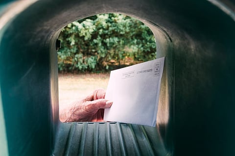 An envolope being taken out of a mailbox.