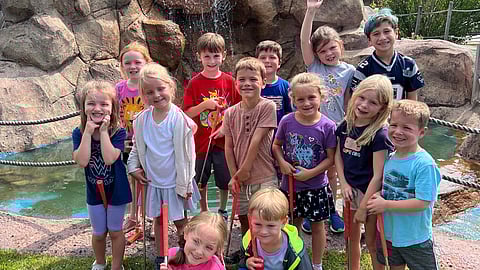 a group of kids hold golf clubs and golf balls on a mini golf course with a waterfall in the background