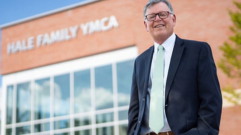 South Shore YMCA CEO Paul Gorman is retiring in 2026 after 16 years of growth, expansion, and community service leadership. image is of a white man in his 60s standing outside an orange brick building