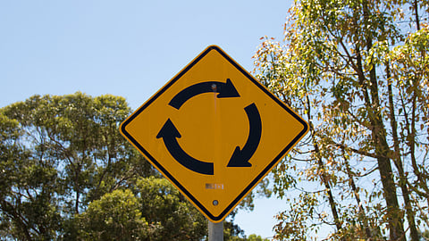 Hingham officials discuss plans for a roundabout to improve safety at a busy intersection near the high school.- image is of a yellow roundabout street sign with blue skies and trees in the background