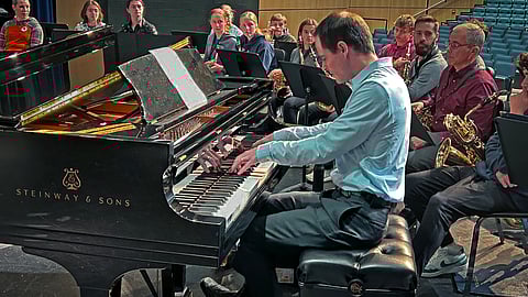 a man plays a piano surrounded by student and professional musicians