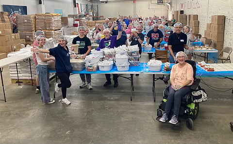 a group of people in a warehouse wearing hair nets packing meals