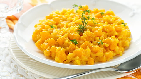 a white bowl holds bright orange pumpkin risotto