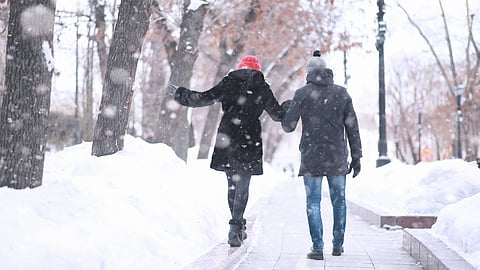 A couple walk hand in hand on a snowy sidewalk
