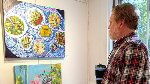 a man stands in front of still life paintings holding a travel mug