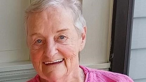 A shoulders-up image of a woman with short white hair and a pink sweater.