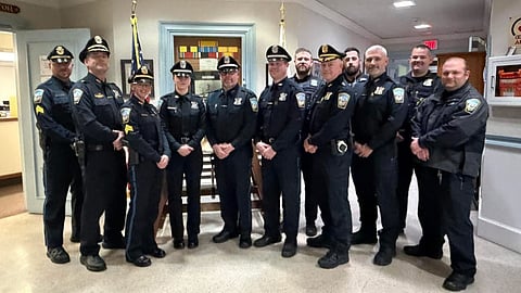 Twelve uniformed police officers stand side by side in a white room.