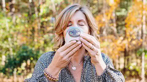 A woman sips bone broth from an earthenware mug outside in the fall leaves