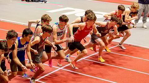 Teenage boys run from the starting line on an indoor track.