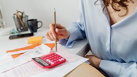 a woman sits at a desk with receipts and a calculator wearing a blue blouse
