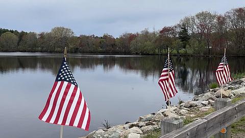 American flags line Jacobs Pond along Main Street in norwell Massachusetts on a cloudy day with trees in the background