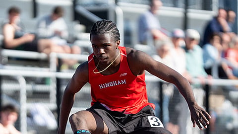 a student athlete leaps over a hurdle wearing a red jersey and black shorts
