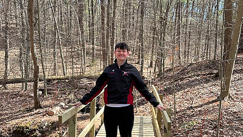 a teenage boy stands on a newly built bridge in the woods