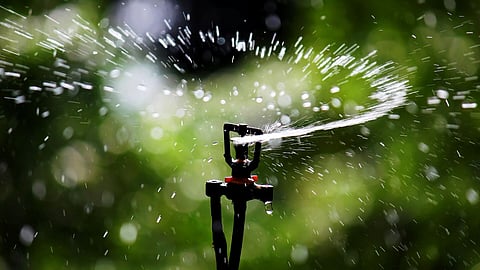 sprinkler spins and sprays water on a green blurry background