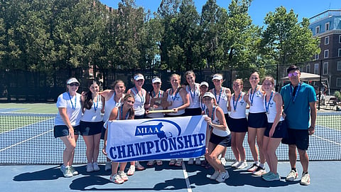 girls tennis team on court poses with MIAA championship banner